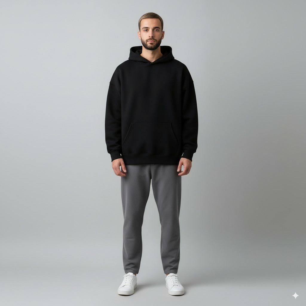 Man wearing a black hoodie and gray pants on a gray background